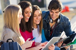 A group of students having fun with smartphones and tablets after class